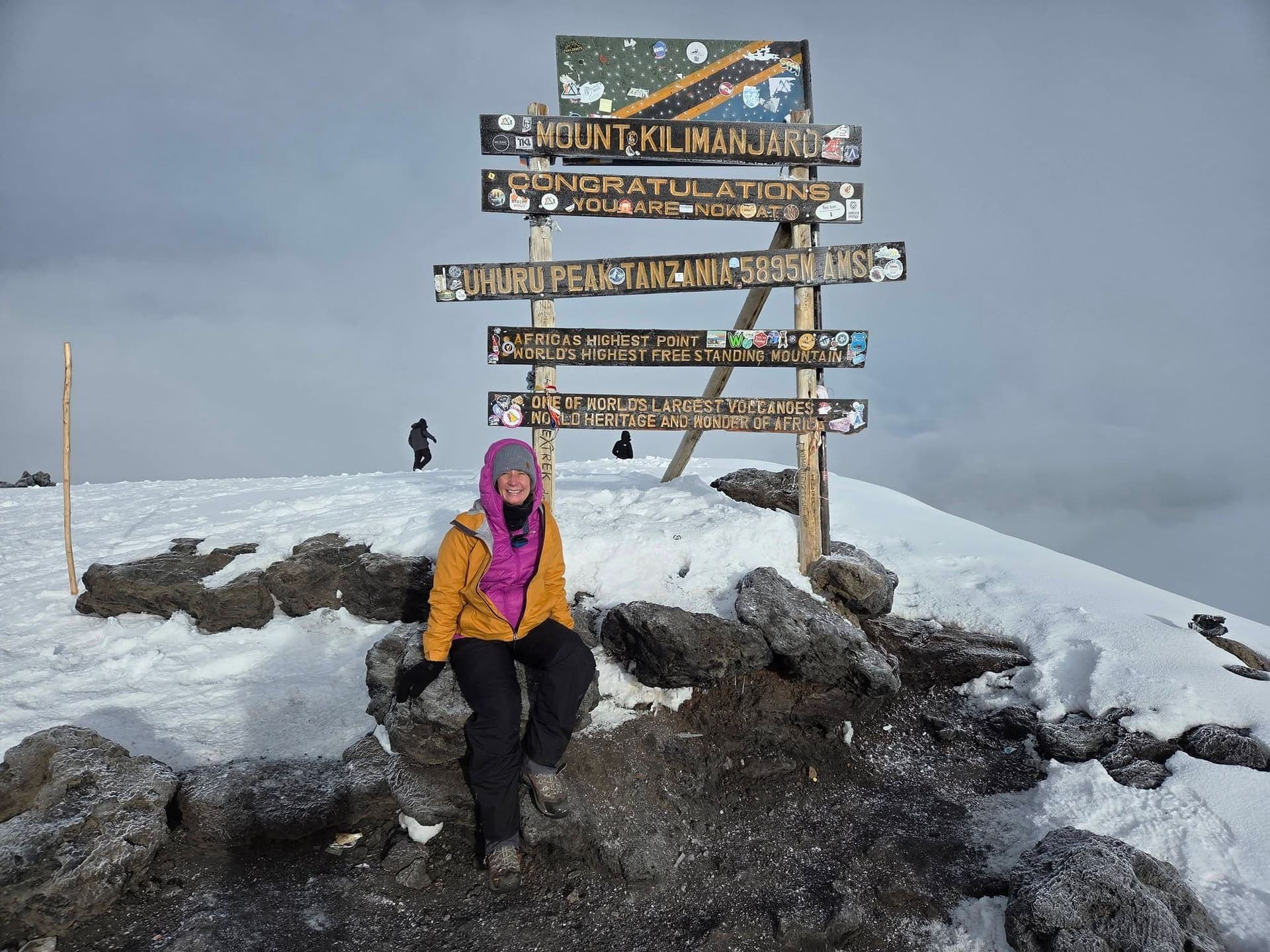 A climber at the Uhuru Peak summit sign in the snow, 5,895 m