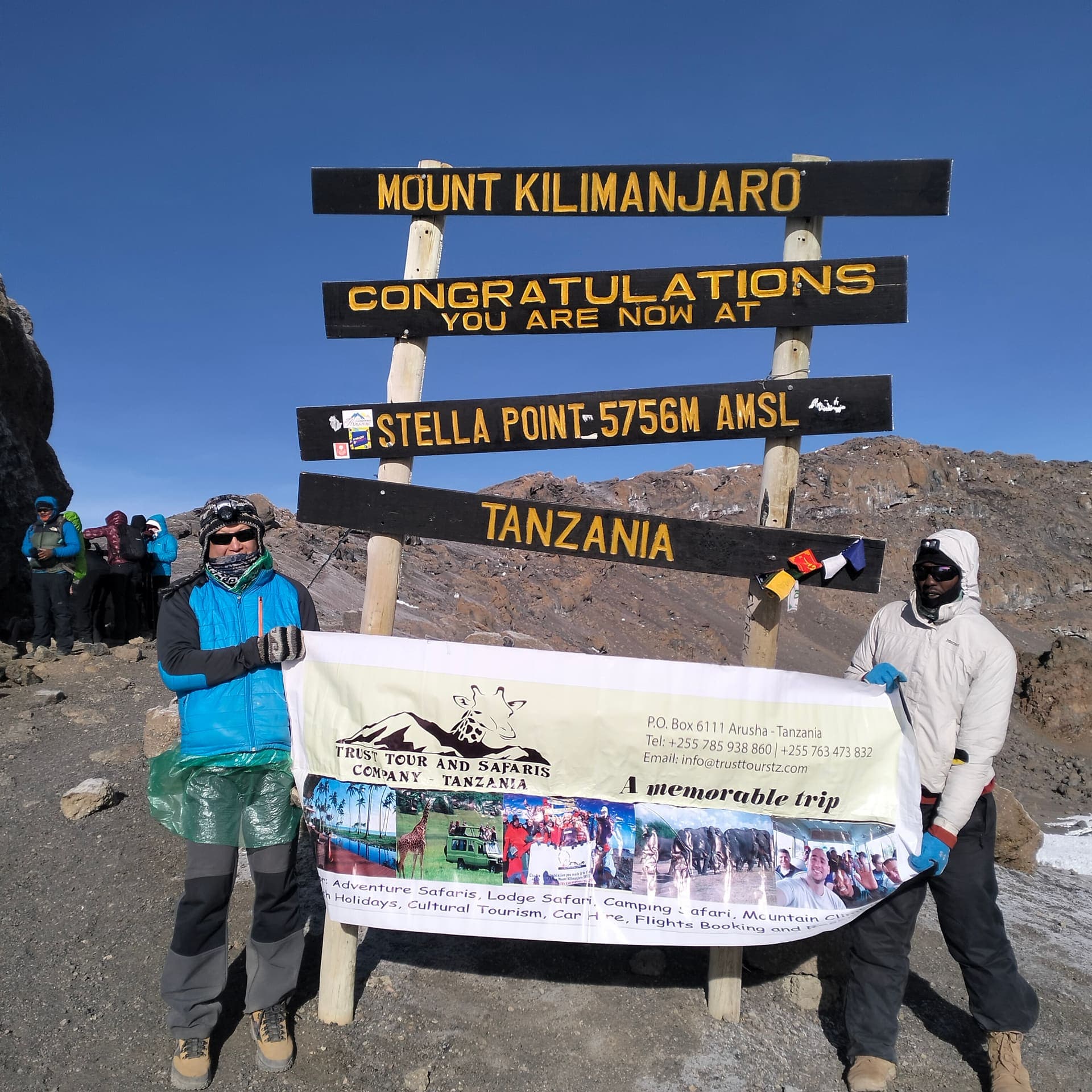 Trust Tours & Safaris climbers holding the company banner at the Stella Point sign on Kilimanjaro